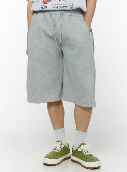 Men's Wide Leg Bermuda Sweat Shorts (Gray) IU529 Gray three-quarter front view on model with hands relaxed at sides showing pleated waist and wide-leg silhouette in heathered fleece fabric