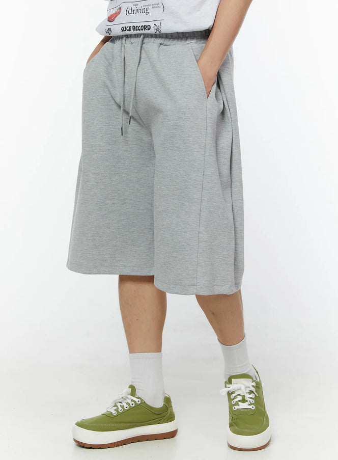 LEWKIN Men's Wide Leg Bermuda Sweat Shorts (Gray) IU529 Gray M/L angled side view on model hands in pockets showing wide-leg silhouette and drawstring waist in heathered cotton fleece