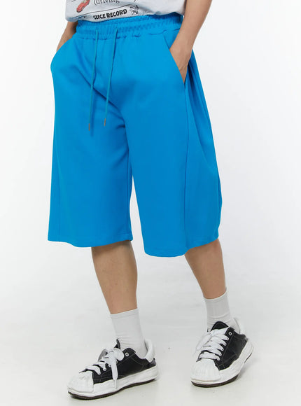 Men's Wide Leg Bermuda Sweat Shorts (Light blue) IU529 Light blue three-quarter front angle on model with hand in pocket showing wide-leg drape and knee-length hem with sneakers