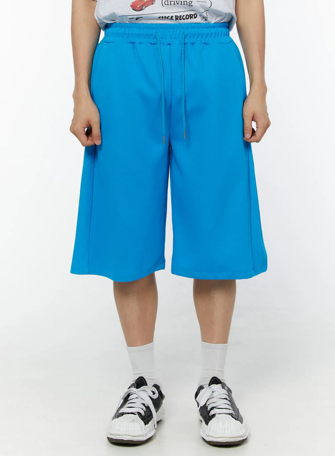 LEWKIN Men's Wide Leg Bermuda Sweat Shorts (Light blue) IU529 Light blue front view on model size M/L with drawstring waist and wide-leg silhouette styled with graphic tee and sneakers
