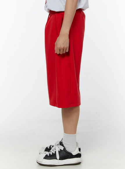 Men's Wide Leg Bermuda Sweat Shorts (Red) IU529 Red back view on model showing clean wide-leg silhouette, elastic waistband, and smooth fabric, paired with white socks and sneakers