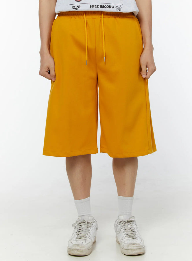 LEWKIN Men's Wide Leg Bermuda Sweat Shorts (Yellow) IU529 yellow front view on model wearing white graphic tee and sneakers, wide-leg silhouette with drawstring waist