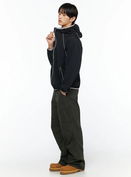 Men's Wide Leg Cargo Pants IL528 dark olive full-body side view on male model styled with black hooded windbreaker hand raised to collar with tan boots