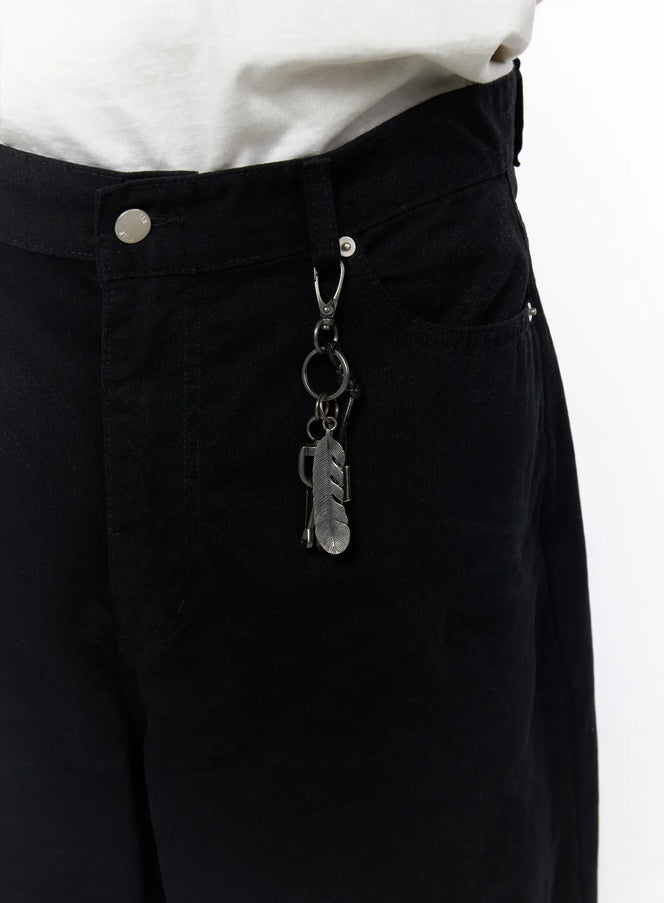 Men's Wide Leg Pants IU523 Black close-up detail of waistband showing metal carabiner clip with feather and ring keychain charm on denim