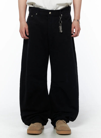 Men's Wide Leg Pants IU523 Black front view on model cropped at waist showing silver rivet detail and metal feather keychain charm