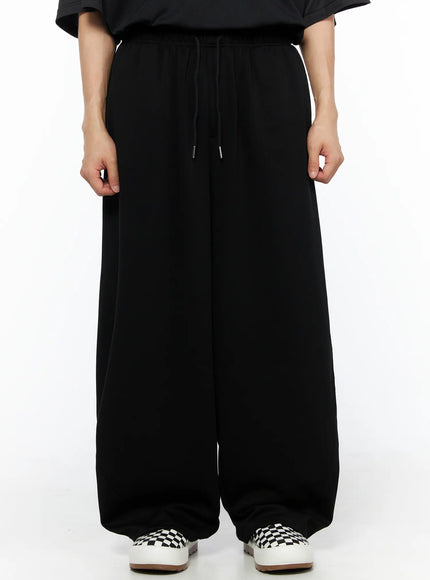 LEWKIN Men's Wide Leg Sweatpants (Black) IL514 black front view on model wearing black tee and checkered slip-on sneakers, elastic drawstring waist, ultra-wide leg silhouette
