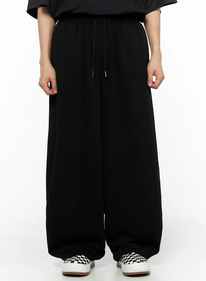 LEWKIN Men's Wide Leg Sweatpants (Black) IL514 black front view on model wearing black tee and checkered slip-on sneakers, elastic drawstring waist, ultra-wide leg silhouette