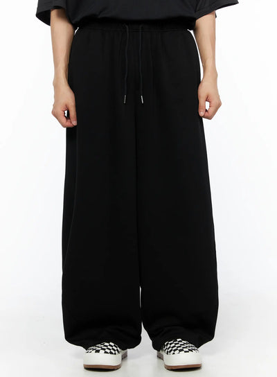 LEWKIN Men's Wide Leg Sweatpants (Black) IL514 black front view on model wearing black tee and checkered slip-on sneakers, elastic drawstring waist, ultra-wide leg silhouette