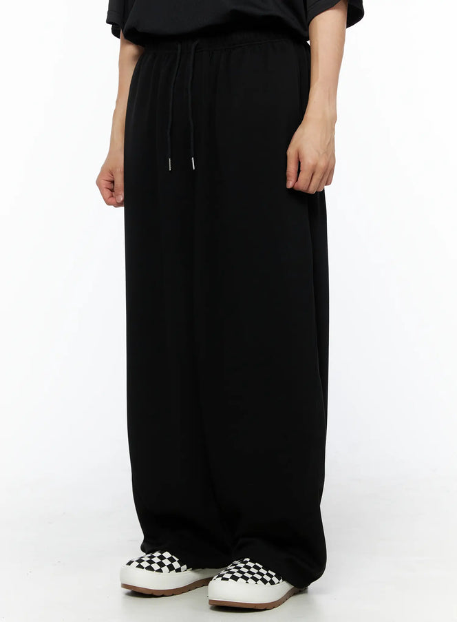 Men's Wide Leg Sweatpants (Black) IL514 black side-angle view on model showing wide-leg drape, drawstring waist, and cargo pocket detail styled with black tee and checkered sneakers