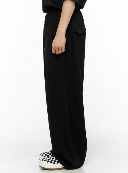 Men's Wide Leg Sweatpants (Black) IL514 black side view on model highlighting single cargo pocket with flap on thigh, drawstring waist, and wide-leg silhouette