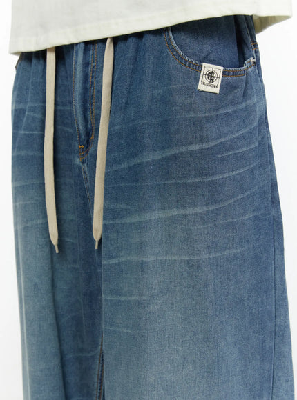Men's Wide Leg Tie-Detail Jeans IL513 Blue close-up detail of front waistband with cream drawstring cream laces brand woven label and washed denim texture