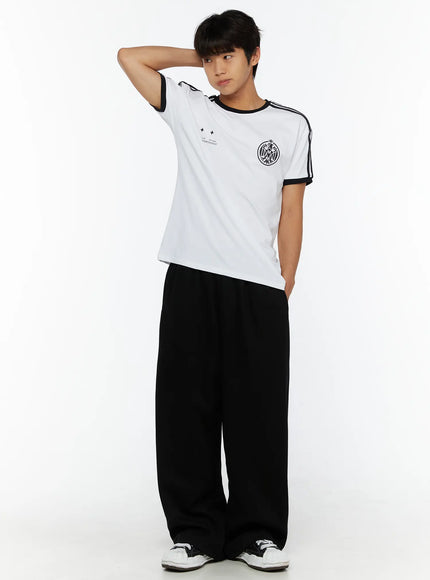 Men's Wide Sweatpants (Black) IL507 Black full-body front shot on male model with hand behind head, styled with striped white graphic tee and sneakers