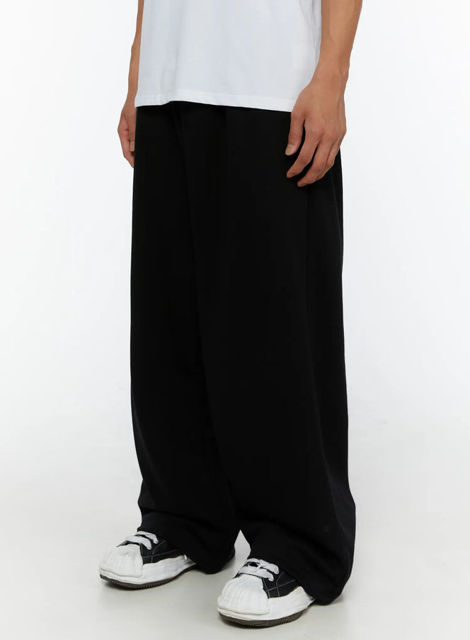 Men's Wide Sweatpants (Black) IL507 Black side shot on male model showing wide-leg drape and length, paired with graphic tee and sneakers