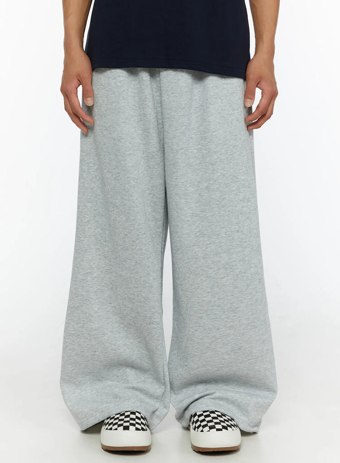 LEWKIN Men's Wide Sweatpants (Gray) IL507 Gray M/L front close-up on male model showing wide-leg heathered fleece fabric and elastic waistband styled with navy tee and checkered sneakers