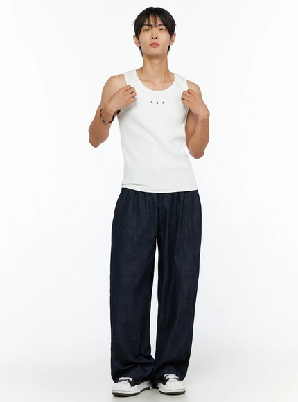 Men's Zack Wide Leg Jeans IL528 Dark blue full-body front on male model wearing white ribbed tank top, hands gripping neckline, elastic drawstring waist denim