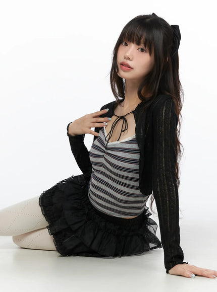 Mesh Tiered Mini Skirt CL522 Black seated pose on model wearing tiered ruffle mini skirt with black cardigan and striped top in relaxed floor pose