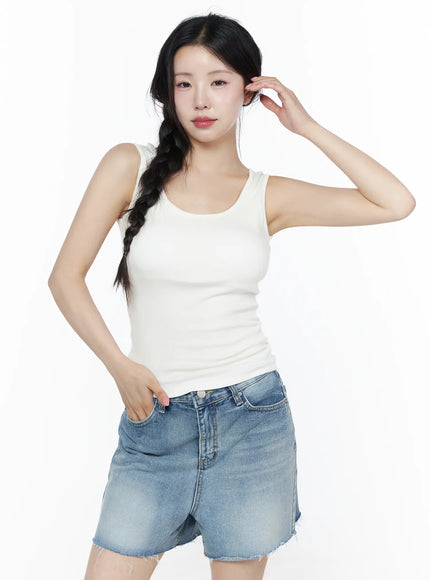 Minimalist Slim-Fit Tank Top IU525 White three-quarter front view on model with hand in hair, scoop neck slim-fit ribbed tank styled with low-rise denim shorts