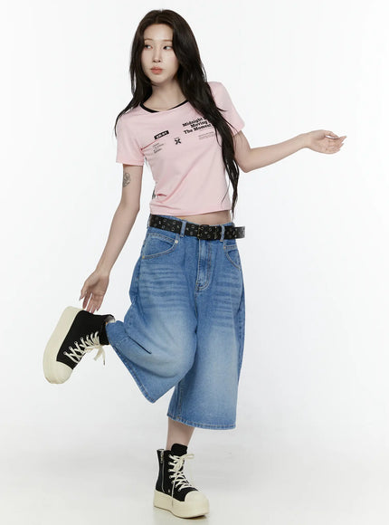 Miu Wide Leg Jeans IL521 Blue full-body front shot on model in dynamic pose holding sneaker one leg raised showing wide-leg denim silhouette with black belt and crop tee