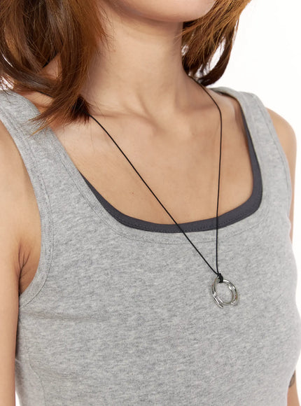Noir Black Cord Necklace IL522 silver side-angle model shot worn over gray tank top, long black cord with spiral ring pendant at chest