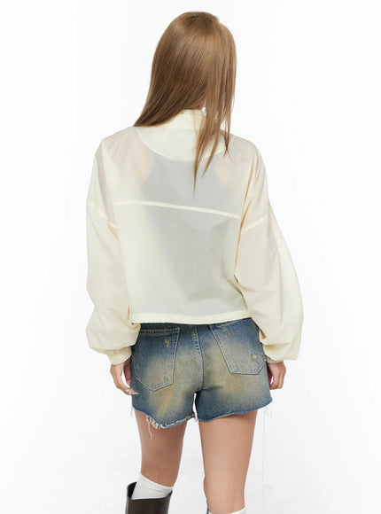 Nylon Cropped Windbreaker CU523 Light beige back model shot, standing rear view showing sheer back panel seam detail, balloon sleeves, cropped waist, styled with denim shorts