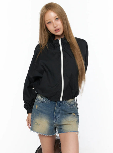 Nylon Cropped Windbreaker CU523 Black front model shot, zip-up cropped windbreaker with white zipper, worn over denim shorts, slight side-turn pose