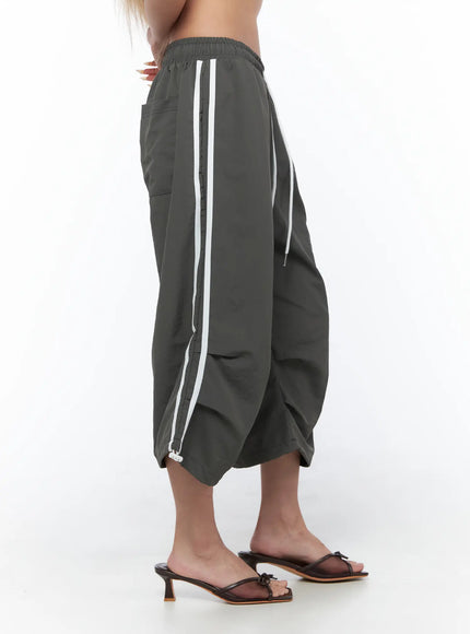 Nylon Track Bermuda Pants CU523 Dark gray side shot on model highlighting dual white side stripes dropped crotch silhouette and hem drawcord
