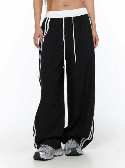 Nylon Track Pants CU523 Black front mid-shot on model showing white waistband, white drawstring, double side stripes, and wide-leg silhouette