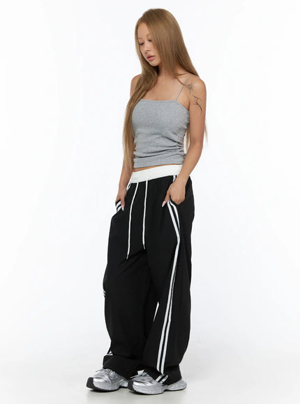 Nylon Track Pants CU523 Black side shot on model looking down, wide-leg silhouette with double white side stripes and white drawstring visible