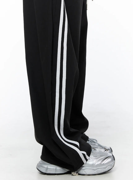 Nylon Track Pants CU523 Black close-up detail of lower leg showing double white side stripe texture and wide hem pooling over silver sneakers