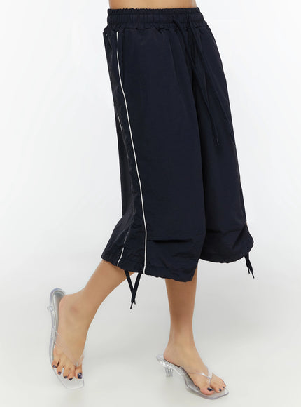 LEWKIN Nylon Wide-Leg Shorts IL524 Dark blue side shot on model showing white piping detail, layered hem, and ankle drawstring ties with clear heels