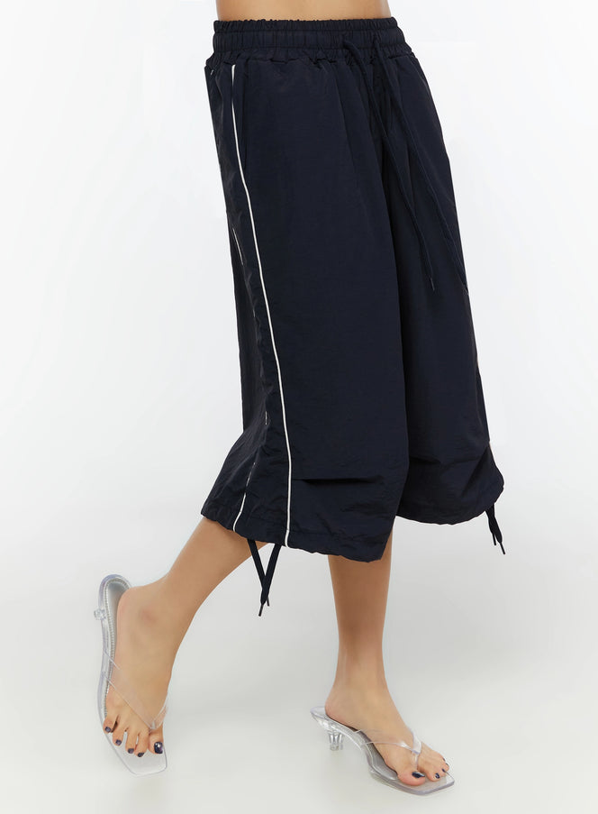 LEWKIN Nylon Wide-Leg Shorts IL524 Dark blue side shot on model showing white piping detail, layered hem, and ankle drawstring ties with clear heels
