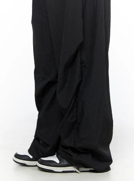 Nylon Wide Pants CL514 Black close-up hem detail showing gathered ankle area with silver snap clasp and crinkled nylon texture with sneakers