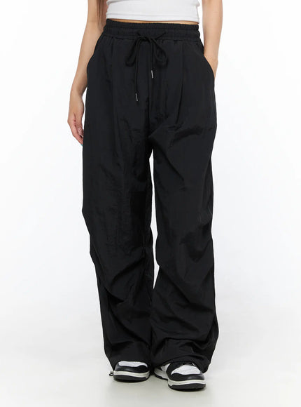 Nylon Wide Pants CL514 Black front view on model with hand in pocket, wide-leg drawstring nylon trousers with crinkled texture and sneakers