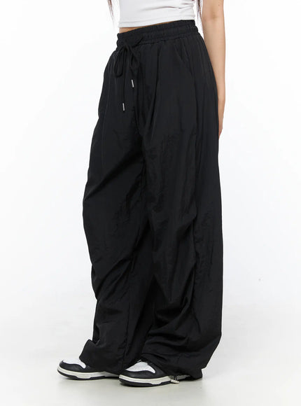 LEWKIN Nylon Wide Pants CL514 Black side view on model wearing white crop top and sneakers, oversized nylon fabric with drawstring waist
