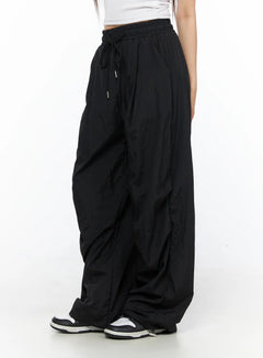 LEWKIN Nylon Wide Pants CL514 Black side view on model wearing white crop top and sneakers, oversized nylon fabric with drawstring waist