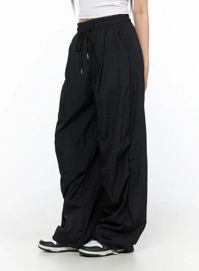 LEWKIN Nylon Wide Pants CL514 Black side view on model wearing white crop top and sneakers, oversized nylon fabric with drawstring waist