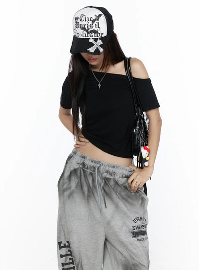 LEWKIN Off-Shoulder Casual Tee CL527 Black S/M front shot on model wearing cap and grey sweatpants, asymmetric off-shoulder neckline, fitted ribbed crop silhouette