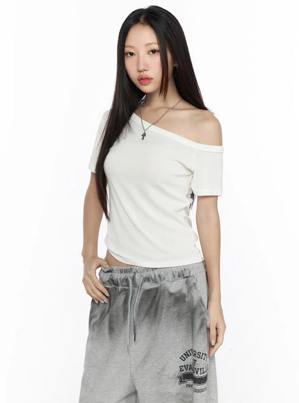 Off-Shoulder Casual Tee CL527 White front three-quarter shot on model, asymmetric off-shoulder neckline, slim crop fit, styled with grey gradient sweatpants