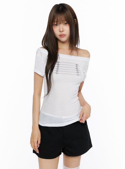 Off-Shoulder Crop Top IL523 White front shot on model standing upright, off-shoulder asymmetric neckline with silver cord detail visible, paired with black denim shorts