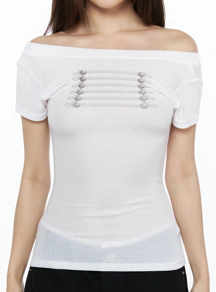 Off-Shoulder Crop Top IL523 White close-up front detail shot on model showing off-shoulder neckline and horizontal silver braided cord with ball-end button embellishment