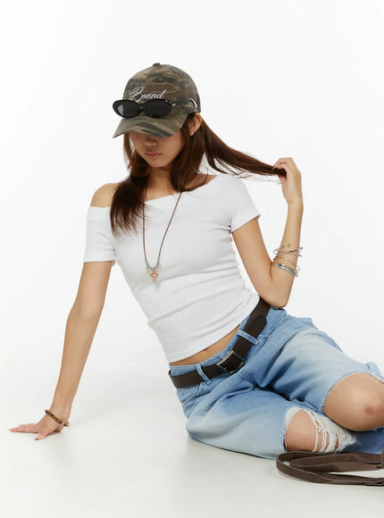 Off-Shoulder Fitted Top CL515 White front model seated on floor leaning forward camo cap necklace and ripped jeans editorial pose