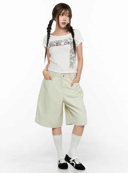 Off-Shoulder Graphic Crop Short Sleeve Tee CL514 White full-body front shot on model with braided pigtails styled with wide-leg beige shorts white socks and black shoes