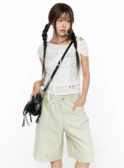 Off-Shoulder Graphic Crop Short Sleeve Tee CL514 White front view on model layered under lace top holding black tassel crossbody bag with beige wide-leg shorts
