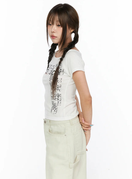 Off-Shoulder Graphic Crop Short Sleeve Tee CL514 White side-profile close-up on model showing fitted body-hugging cut and Cyrillic graphic lettering styled with beige shorts