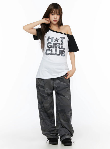Off-Shoulder Graphic Print Top IL523 White full-length front shot on model with one hand raised to hair black raglan sleeves star studs camo pants