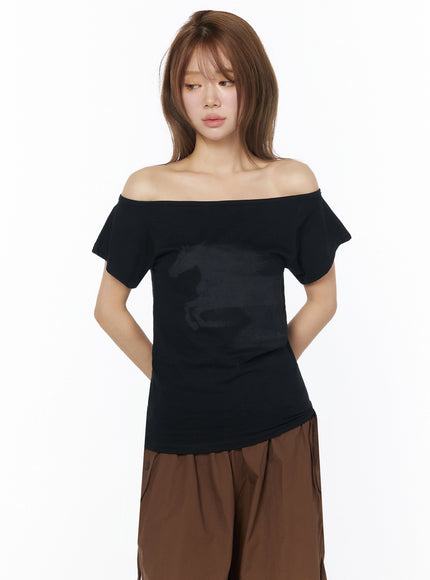 Off-Shoulder Graphic Short Sleeve Top IU525 Black front shot on model with hands behind back, horse graphic print on cotton fabric, paired with brown wide-leg pants