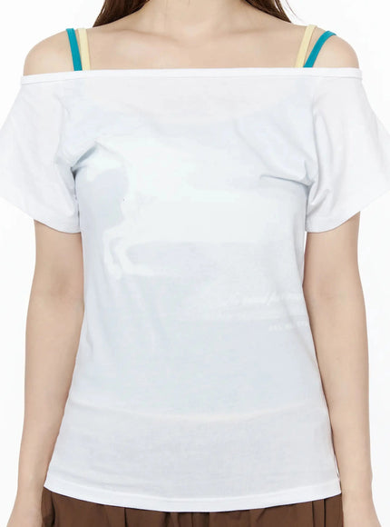 Off-Shoulder Graphic Short Sleeve Top IU525 White close-up detail shot on model showing off-shoulder square neckline, colorful teal and beige layered bra straps, horse graphic