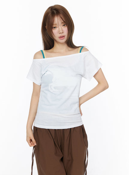 Off-Shoulder Graphic Short Sleeve Top IU525 White front shot on model with hand on hip, fitted cotton tee with off-shoulder neckline and colorful layered strap detail