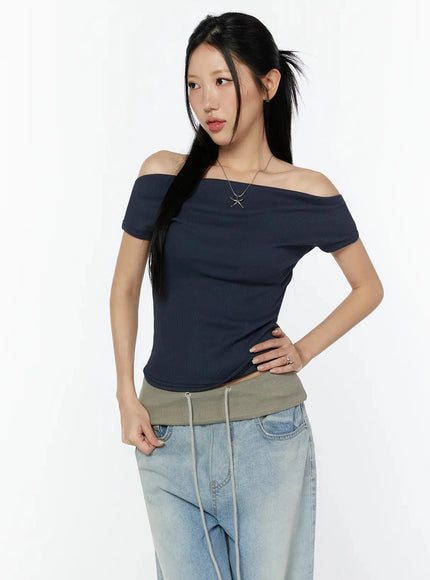 Off-Shoulder Ribbed Short Sleeve Top IU524 Dark blue three-quarter front model shot hand on hip showing fitted ribbed body and off-shoulder neckline with silver necklace