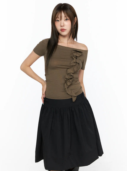 Off-Shoulder Ruffle Tee CL517 Dark beige front shot on model with hand on hip, fitted off-shoulder silhouette and ruffle detail, styled with black gathered midi skirt